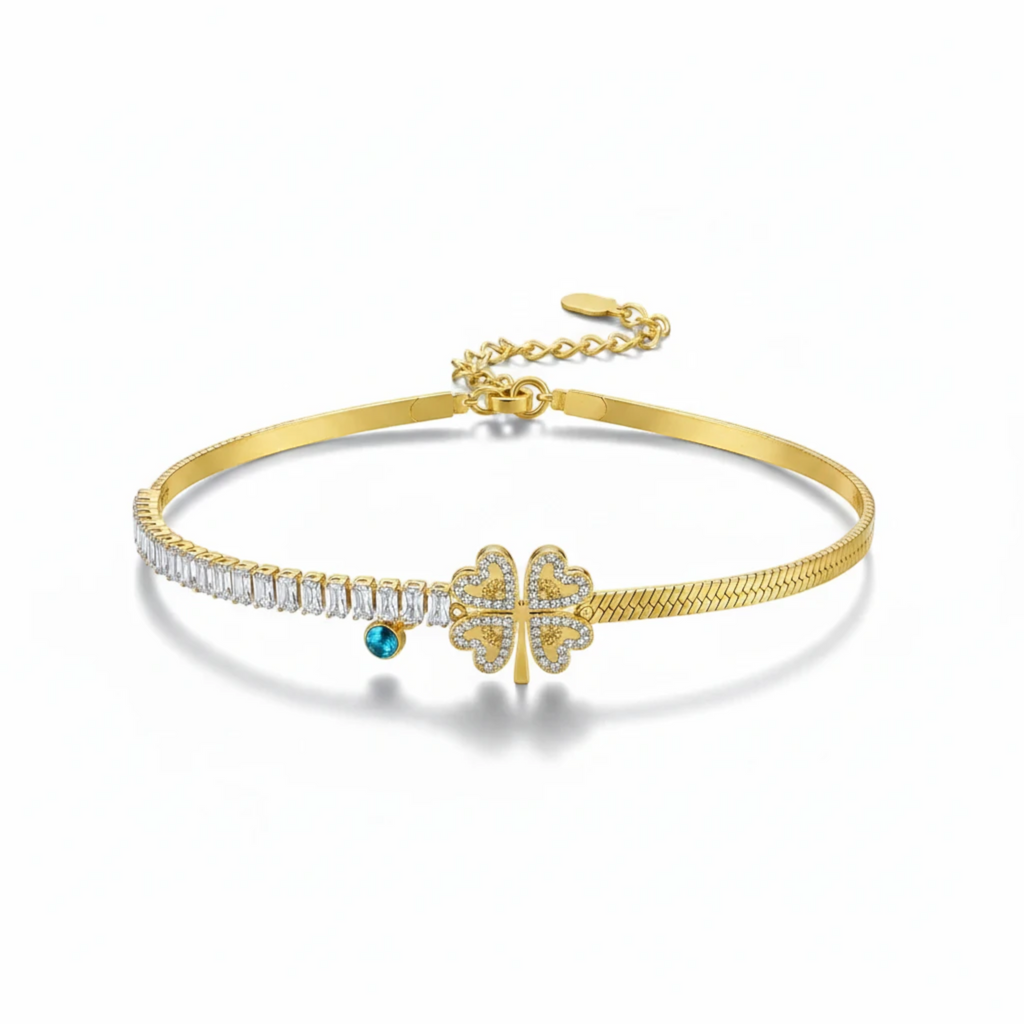 MiRA armband i guldtonat rostfritt stål med fyrklöver, gnistrande stenar och en blå detalj.