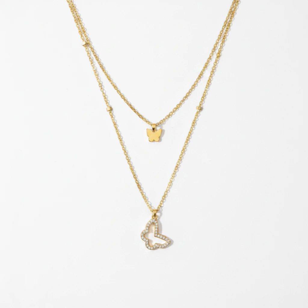 MiRA dubbelt halsband i guldton med en minimalistisk fjäril och en större fjäril prydd med gnistrande stenar.