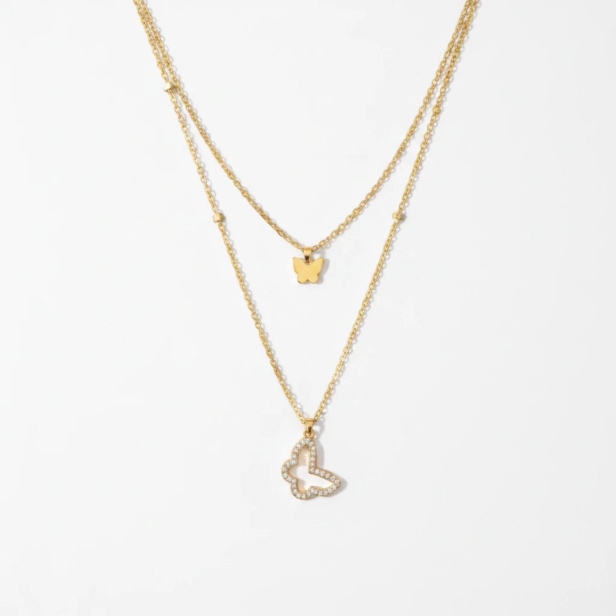 MiRA dubbelt halsband i guldton med en minimalistisk fjäril och en större fjäril prydd med gnistrande stenar.