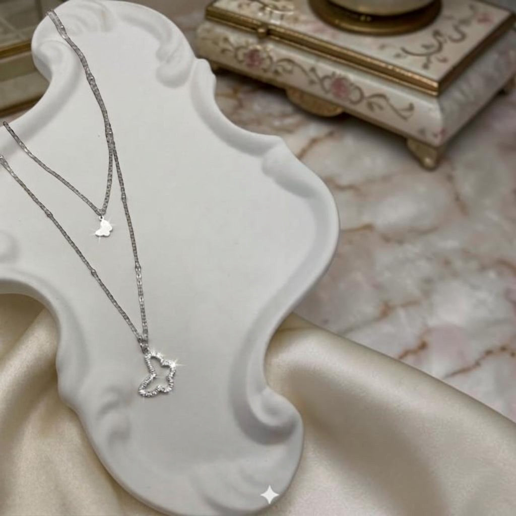 MiRA dubbelt halsband i silvertonad metall med två fjärilshängen, varav ett är dekorerat med gnistrande stenar.