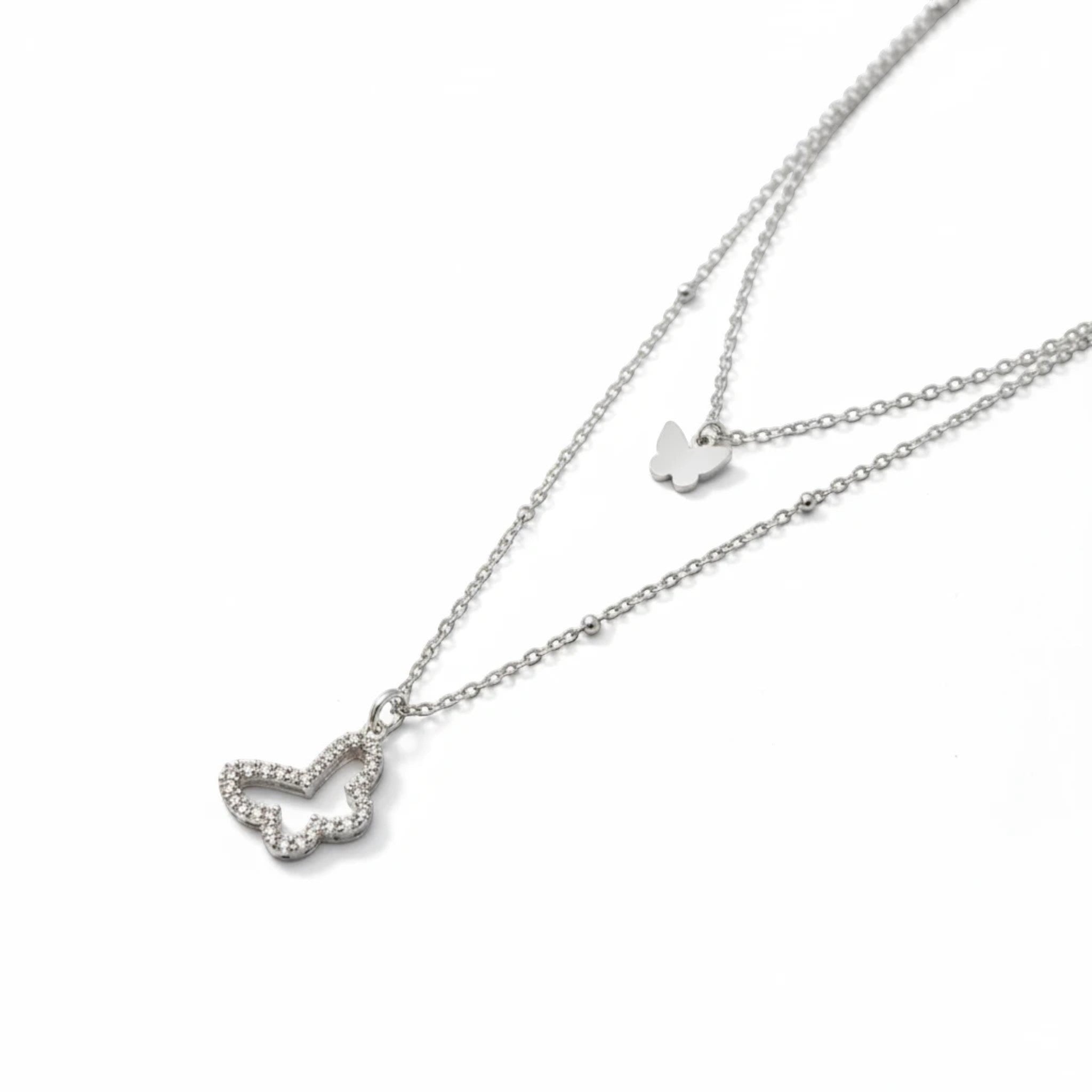 MiRA dubbelt halsband i silvertonad metall med en liten slät fjäril och en större fjäril prydd med gnistrande stenar.