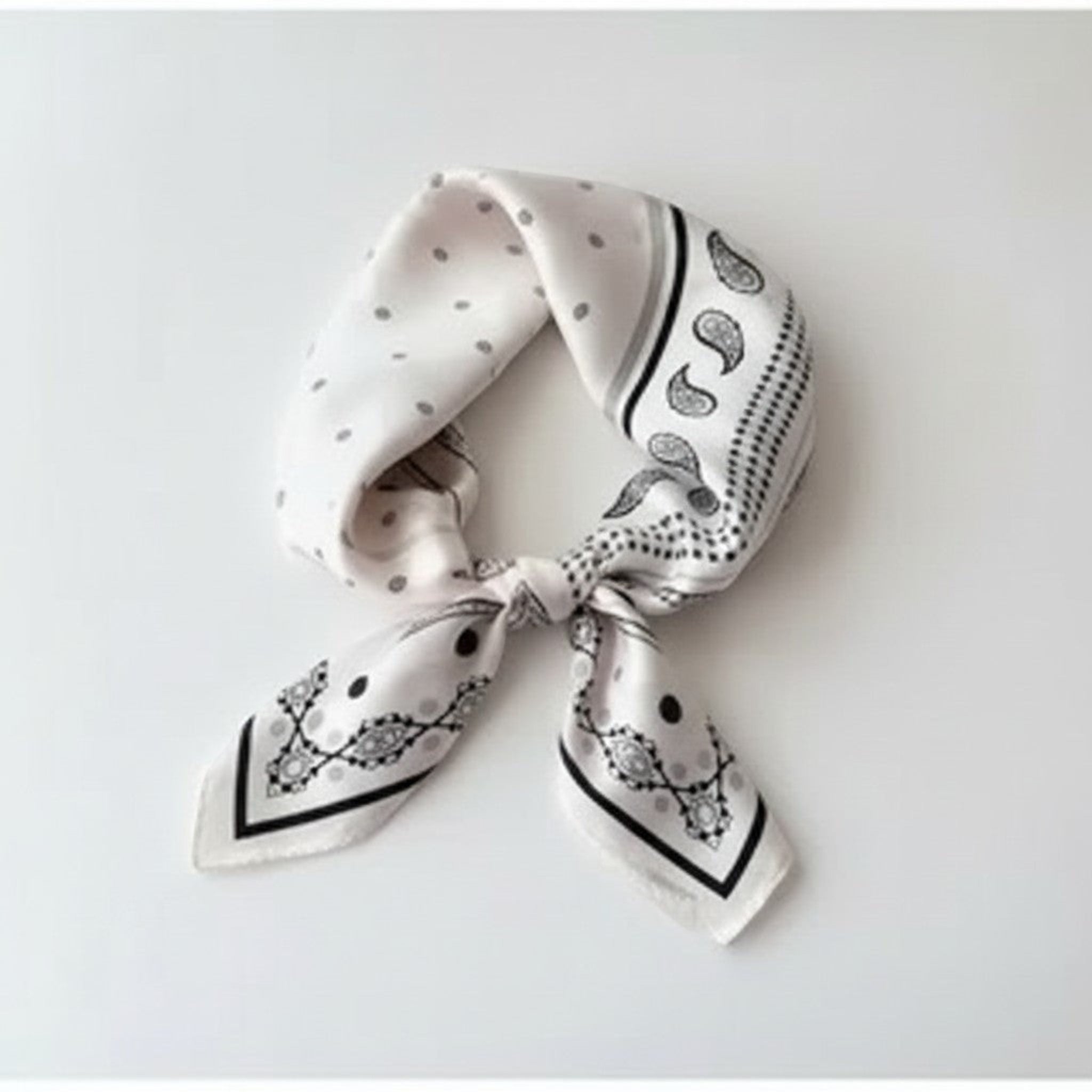 MiRA fyrkantig scarf i sidenliknande material med svartvitt mönster av prickar och paisley, knuten som en halsduk.
