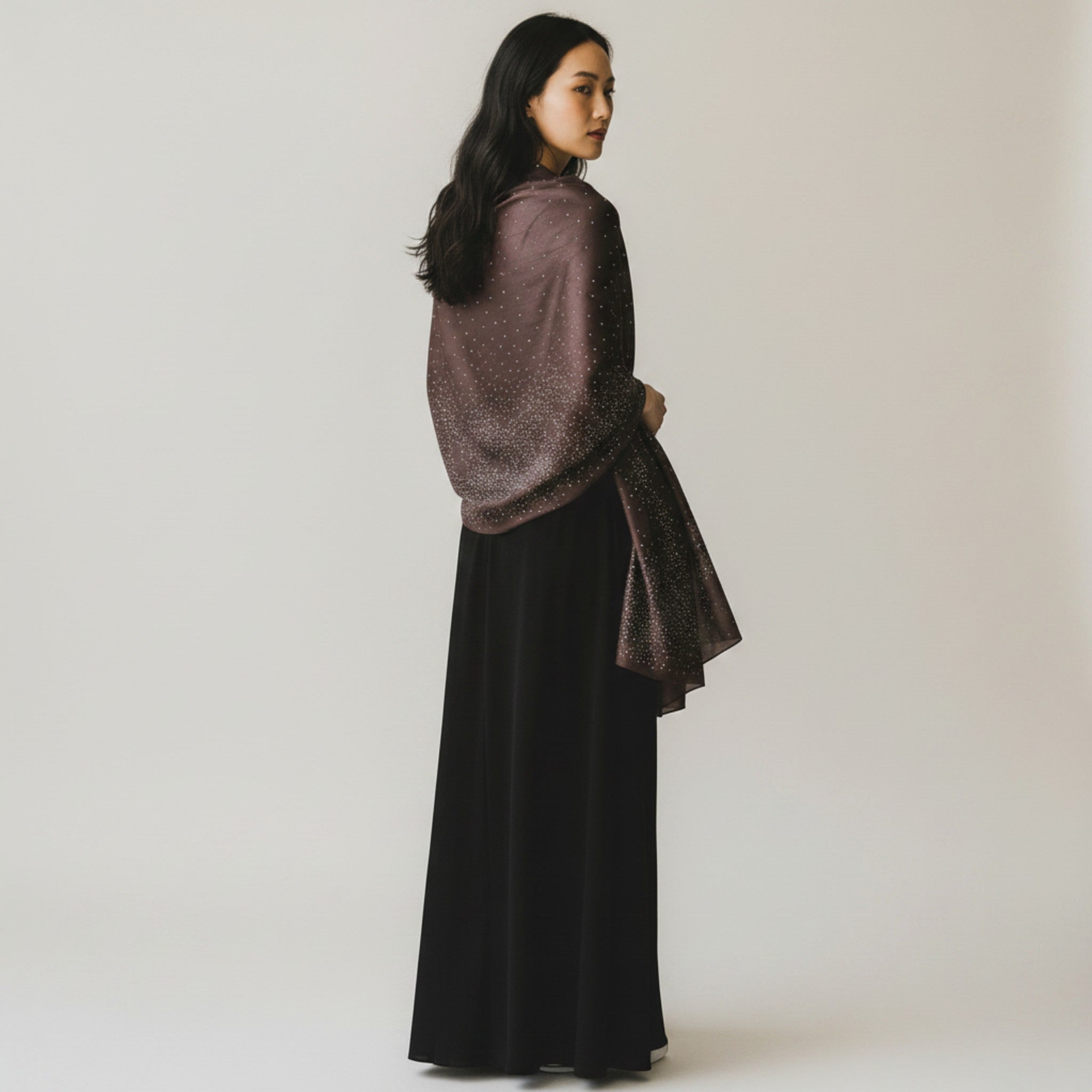 MiRA grå sjal i polyester med glittriga detaljer draperad över axlarna på en kvinna i lång svart klänning
