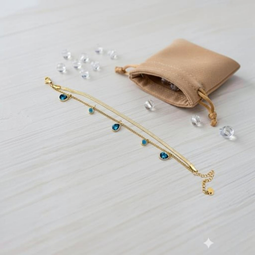 MiRA guldpläterat armband i 316L stål med blå evil eye-detaljer och pansarkedja på en ljus träyta.