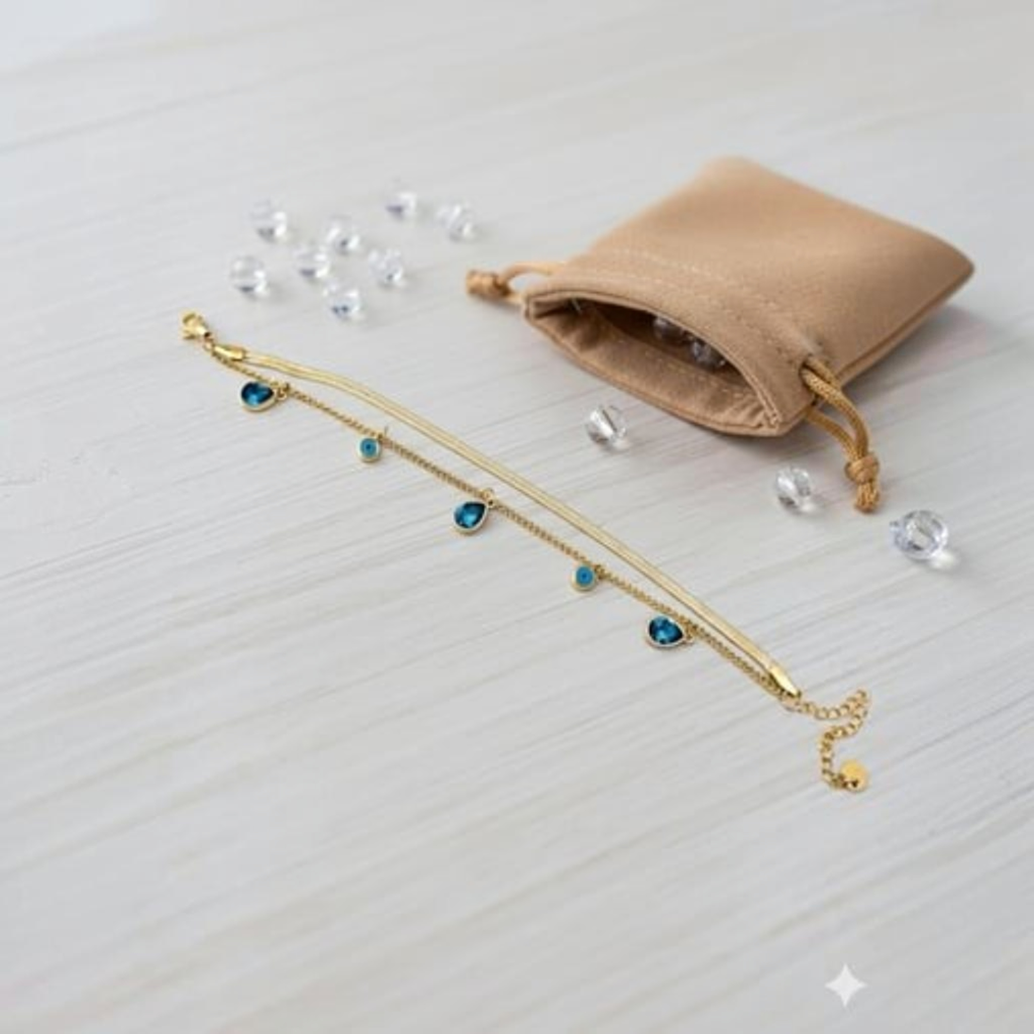 MiRA guldpläterat armband i 316L stål med blå evil eye-detaljer och pansarkedja på en ljus träyta.