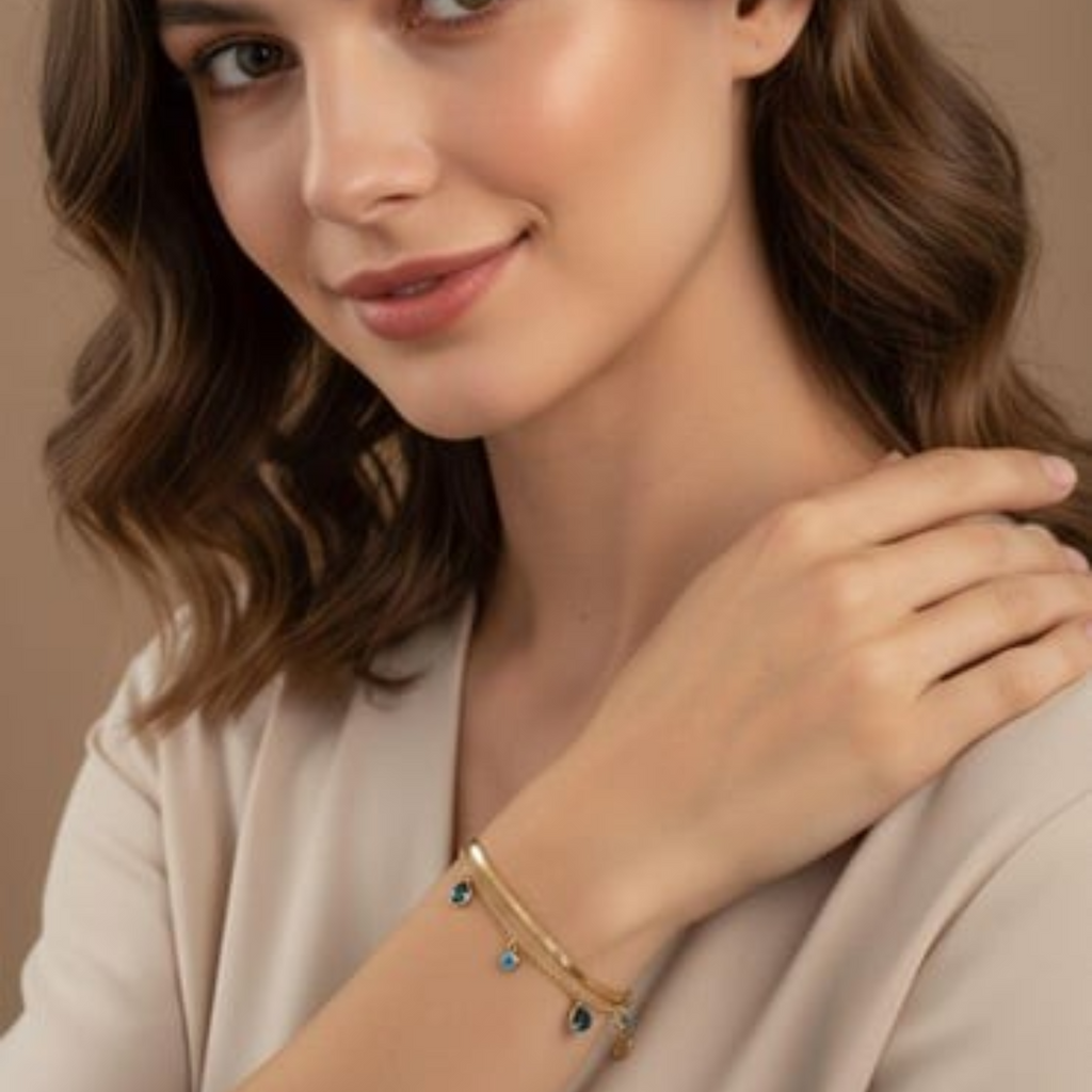 MiRA guldpläterat armband i 316L stål med blå evil eye-detaljer buret av en kvinna i beige topp.
