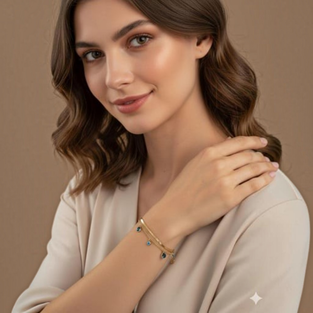 MiRA guldpläterat armband i 316L stål med blå evil eye-detaljer på en kvinna i beige topp.
