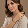 MiRA guldpläterat armband i 316L stål med blå evil eye-detaljer på en kvinna i beige topp.