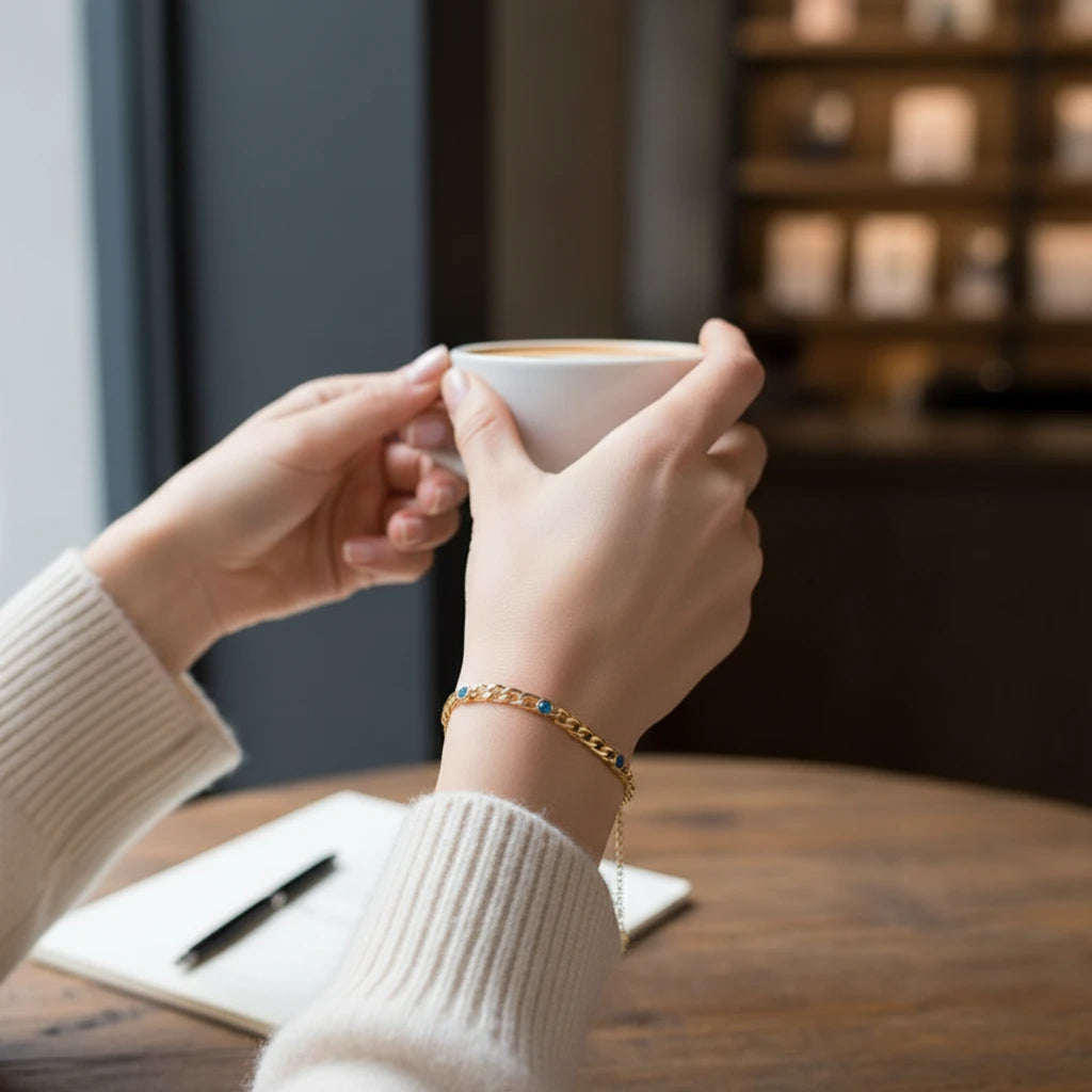 MiRA elegant guldarmband i rostfritt stål med blå cirkulära detaljer på en person som håller en kaffekopp