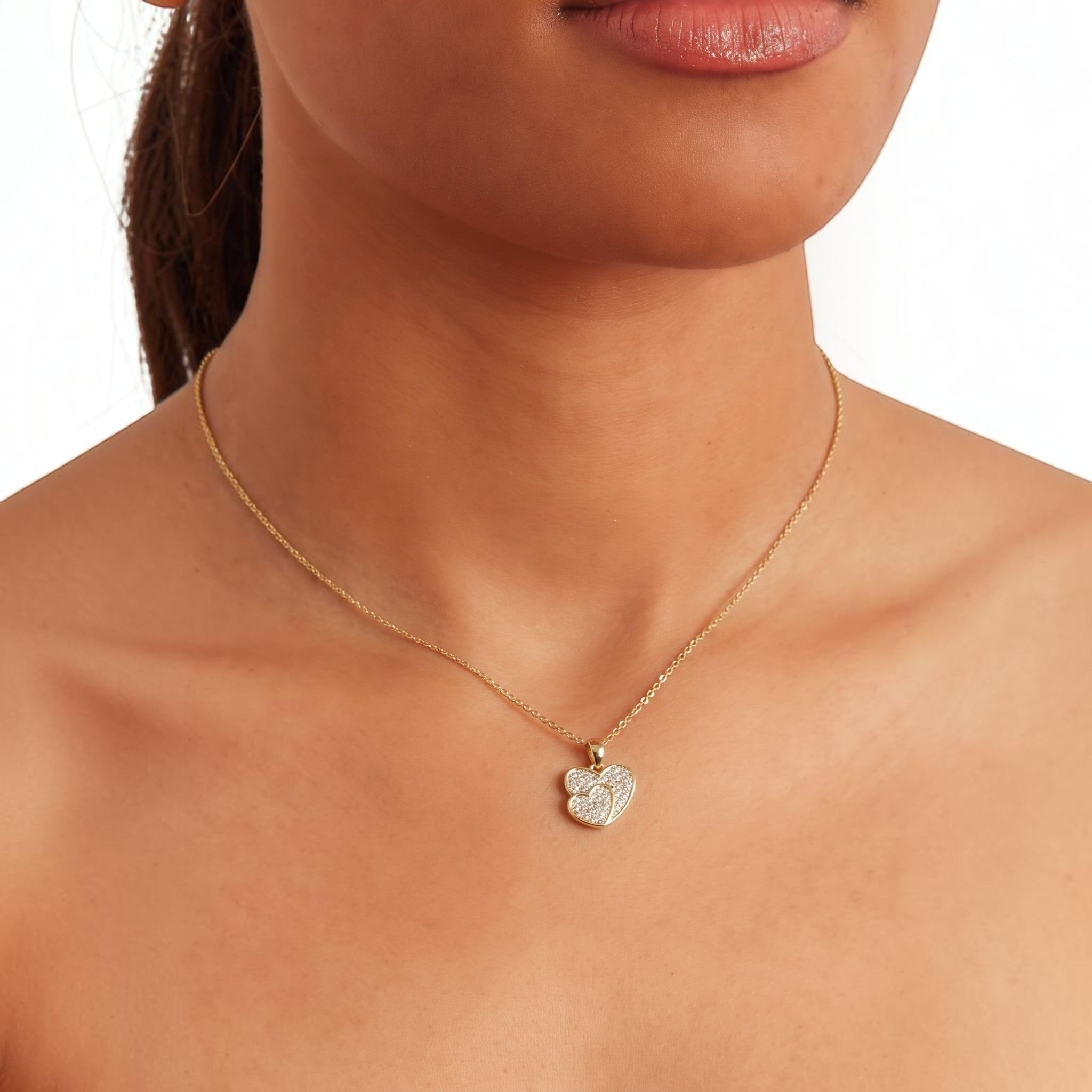 MiRA halsband i guld med ett hjärtformat hänge prytt med gnistrande stenar runt en kvinnas hals.