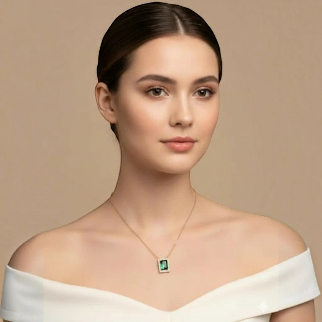 MiRA halsband i guld med rektangulärt grönt hänge buret av en kvinna i vit axelbandslös topp