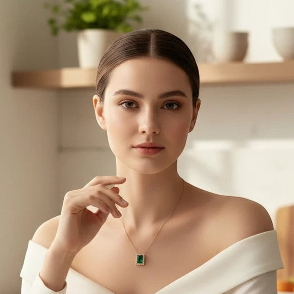 MiRA halsband i guld med rektangulärt grönt hänge buret av kvinna i vit topp i ett ljust kök.