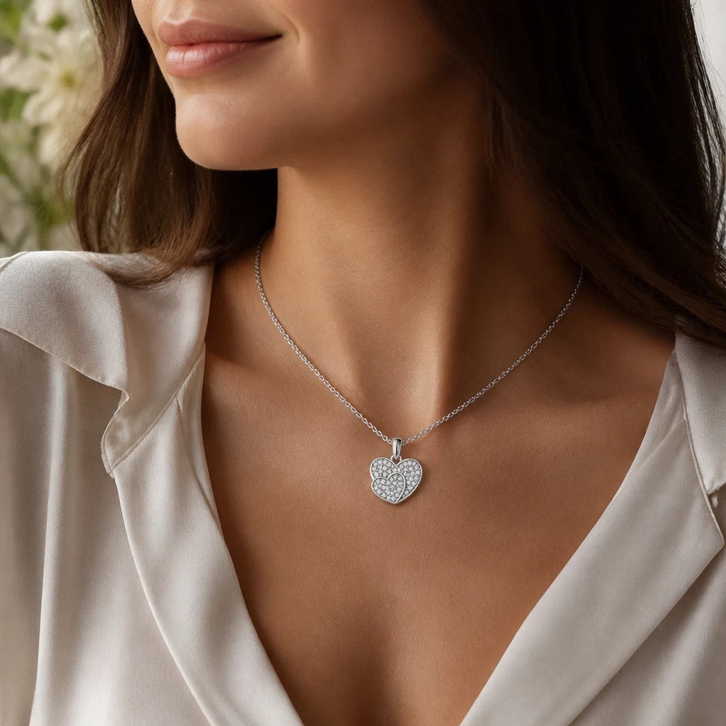 MiRA halsband med dubbla hjärtan i silvertonad metall prytt med gnistrande stenar buret av en kvinna.