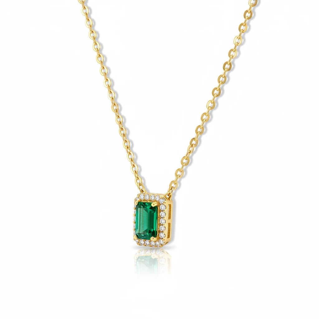 MiRA halsband i guld med rektangulär grön sten omgiven av gnistrande små kristaller på en tunn kedja.
