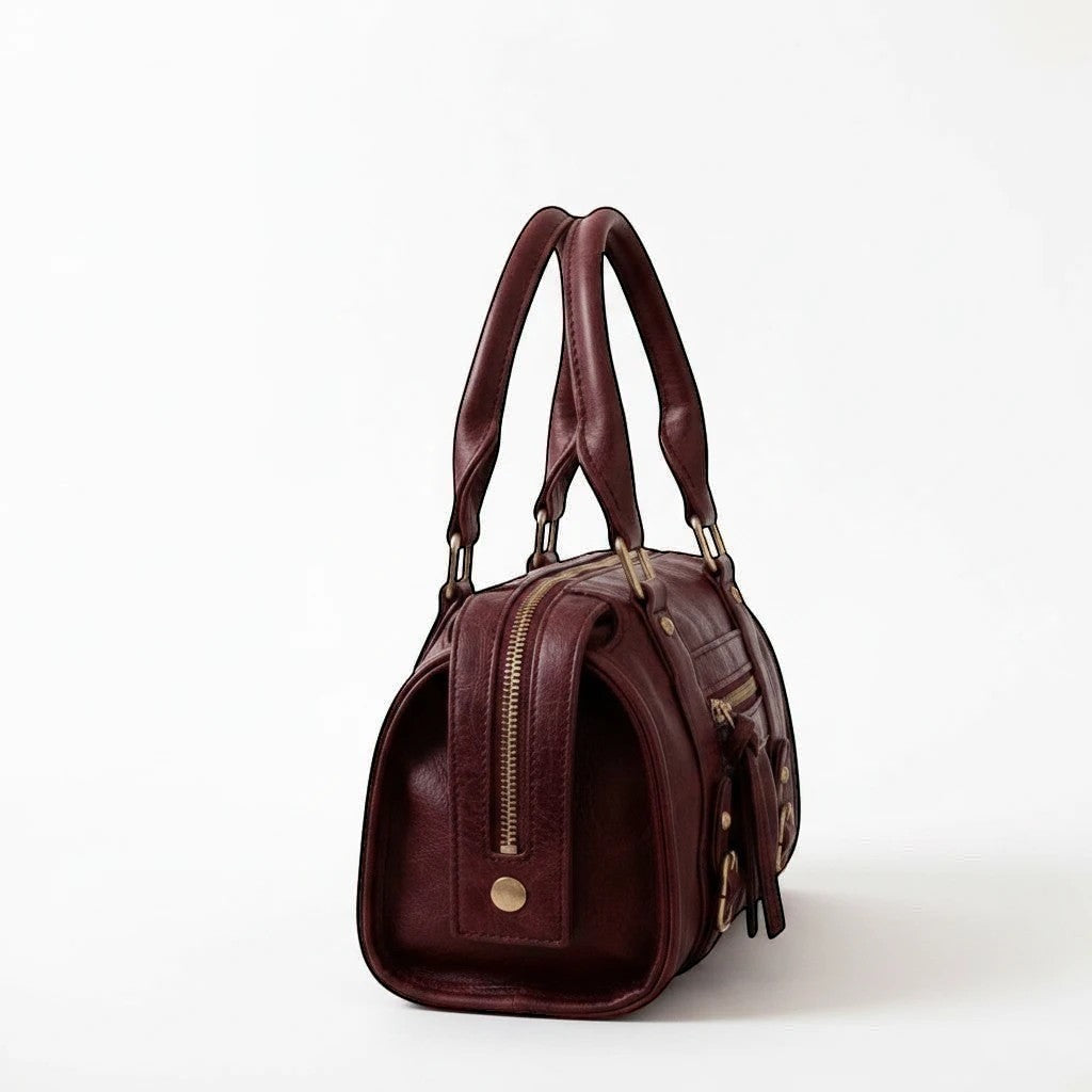 MiRA handväska i konstläder med guldfärgade metalldetaljer och dragkedja, sedd från sidan.