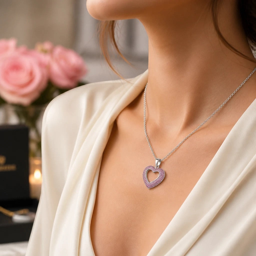MiRA hjärtformat halsband i silver med gnistrande rosa stenar buret av en kvinna i elegant vit blus.