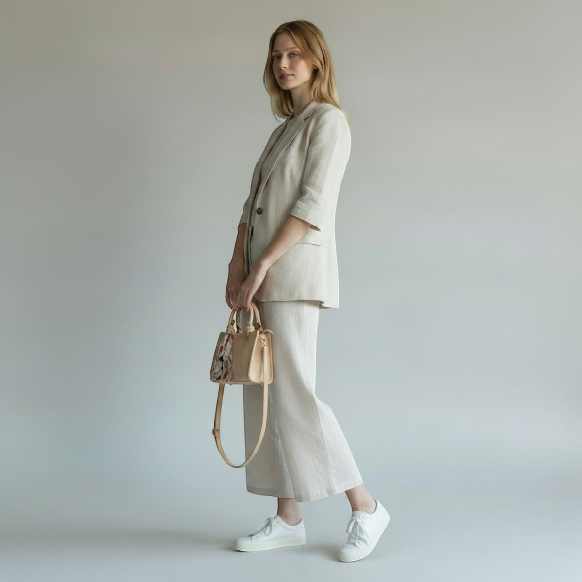 MiRA krämvit axelväska i veganskt läder med plisserad textur och dekorativ scarf, buren av modell i beige kostym.
