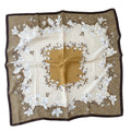 MiRA kvadratisk sjal med blommigt mönster i beige, guld och mörkbrunt med en elegant ram och mjuk lyster.