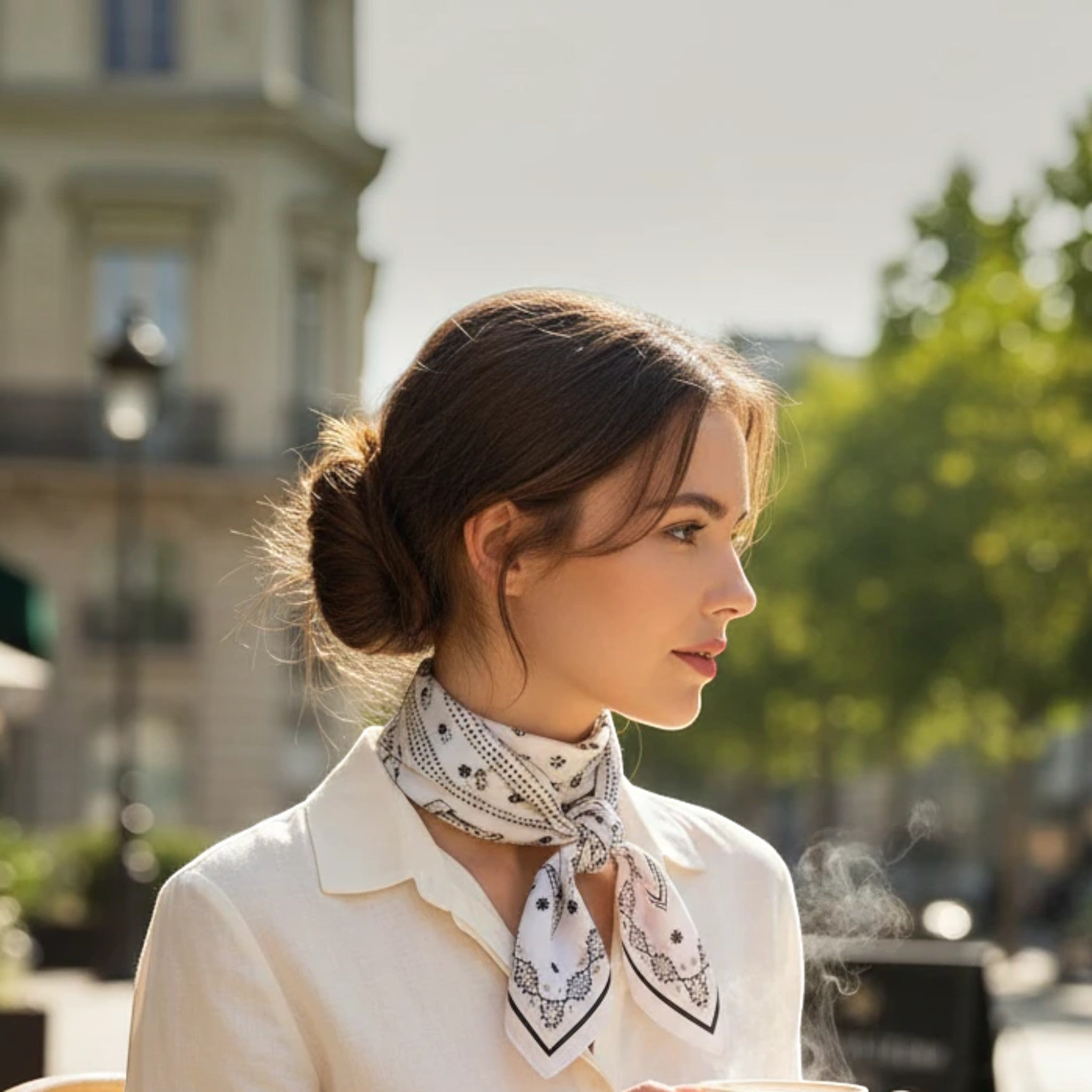 MiRA elegant fyrkantig scarf i vitt och svart med mönster, buren knuten runt halsen av en kvinna utomhus.