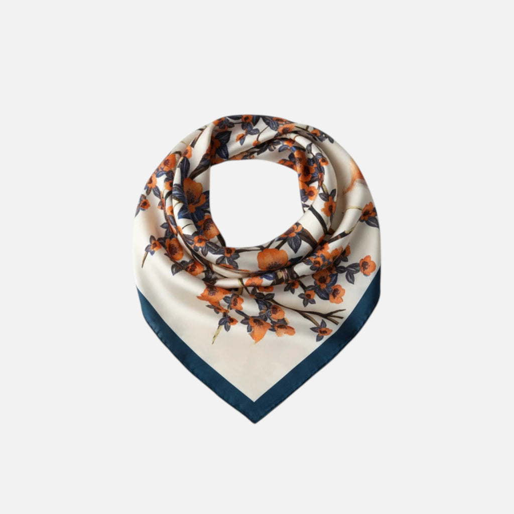 MiRA mönstrad scarf i polyester med blommigt motiv i orange och vitt på ljus botten med mörkblå kant.