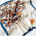 MiRA mönstrad scarf i polyester med blommigt motiv i orange och blått på en krämvit bakgrund med mörkblå kant.