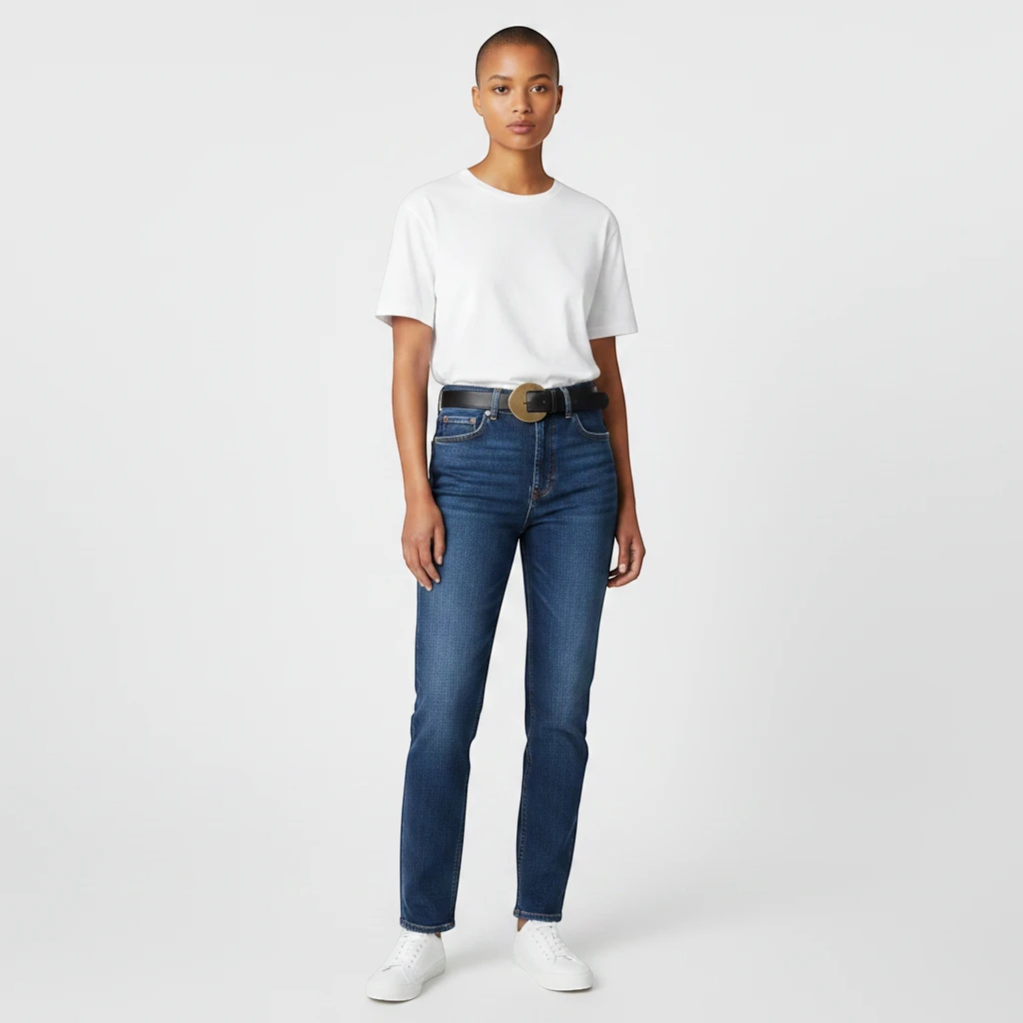 MiRA svart damskärp i veganskt läder med runt guldspänne, buret av en modell i jeans och vit t-shirt.