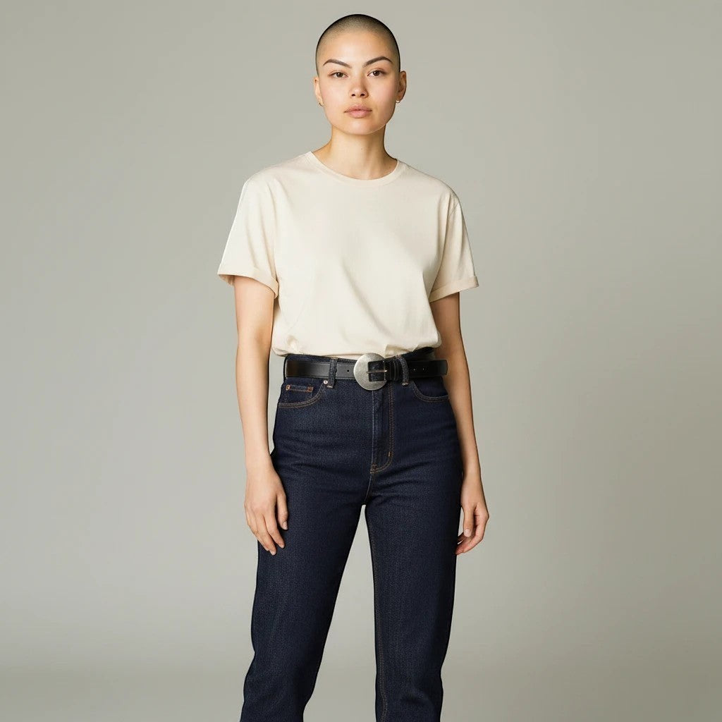 MiRA svart skärp i veganskt läder med guldigt spänne buret av en modell i beige t-shirt och mörka jeans