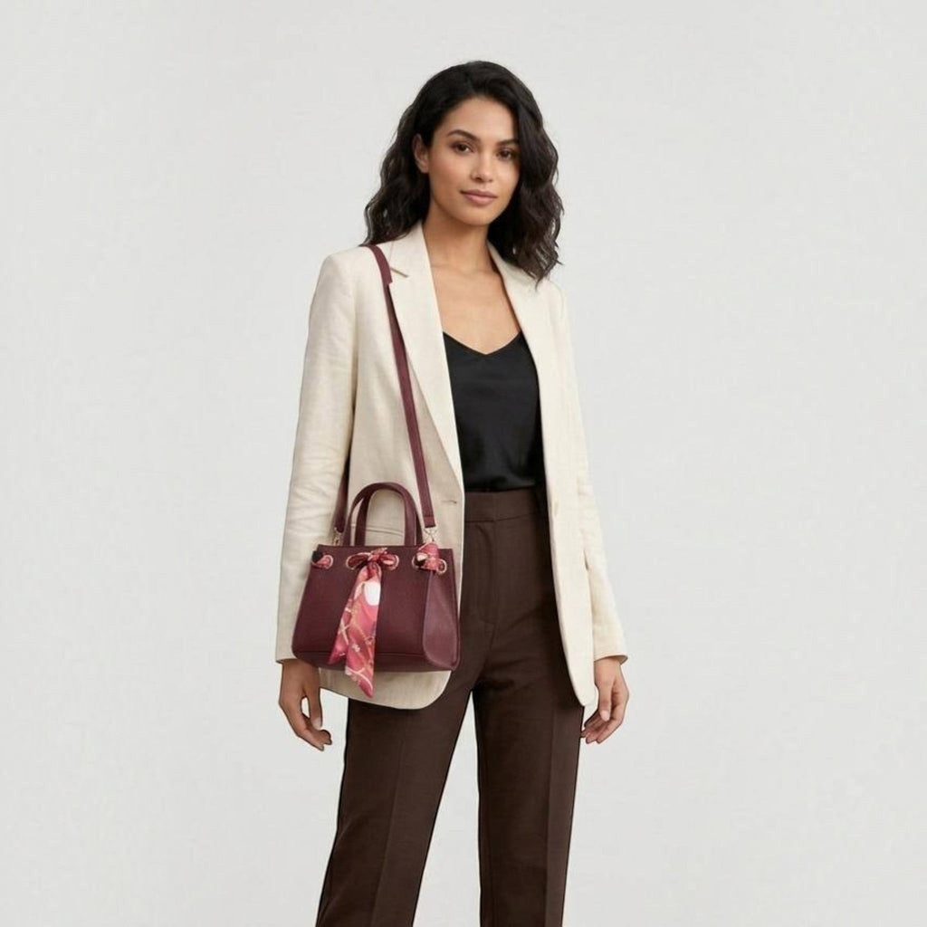 MiRA handväska i vinrött veganskt läder med dekorativ scarf, buren som crossbody-väska av en kvinna i kavaj.